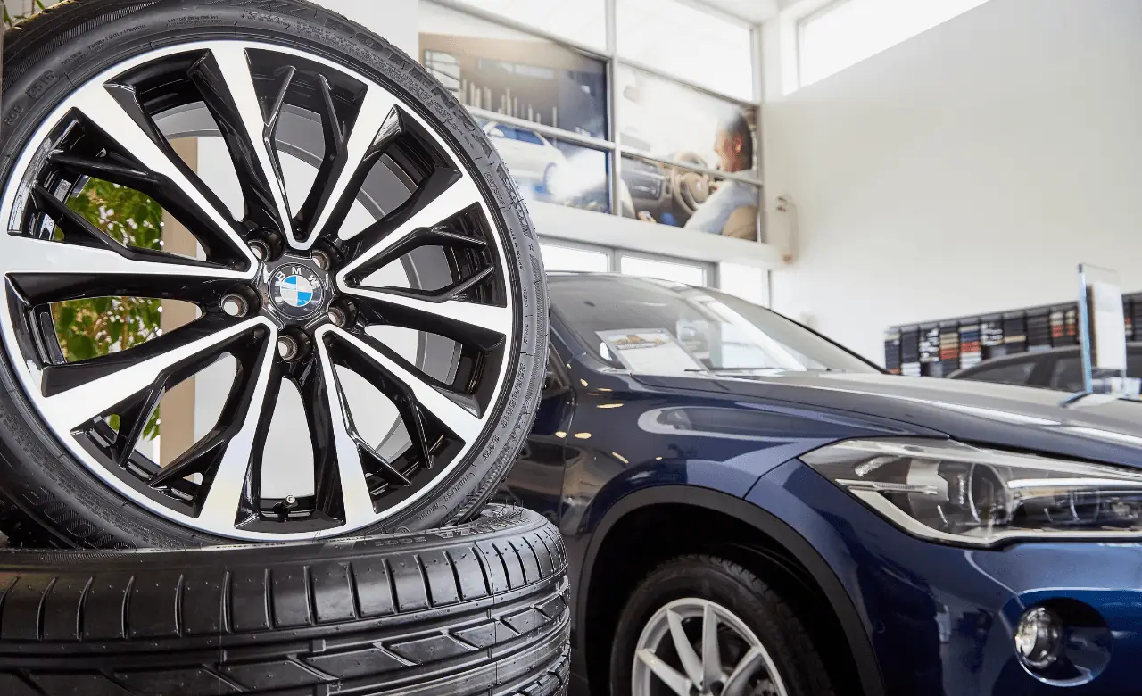 Close-up of car tires stacked beside a stylish blue vehicle in a Guelph showroom. Display windows and car-themed wall art highlight the sleek, modern setting, reflecting excellence in European car maintenance. Euro Mechanic | Brock Road Garage Guelph | Top Reviewed Auto Repair Shop in Guelph | Visit brockroadgarage.ca