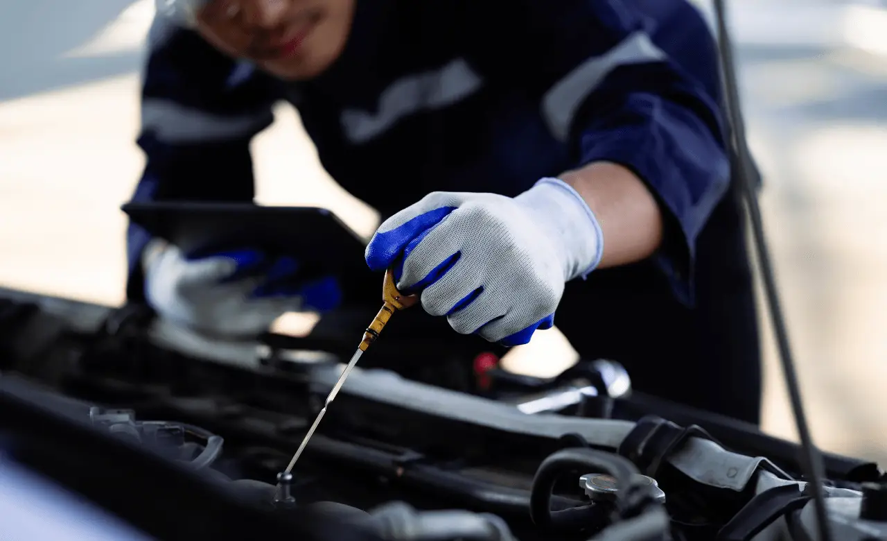 A mechanic in Guelph checks the oil level of a European car engine using a dipstick. The person, donned in white gloves with blue accents, holds a digital tablet, focusing on the dipstick and engine area. Euro Mechanic | Brock Road Garage Guelph | Top Reviewed Auto Repair Shop in Guelph | Visit brockroadgarage.ca