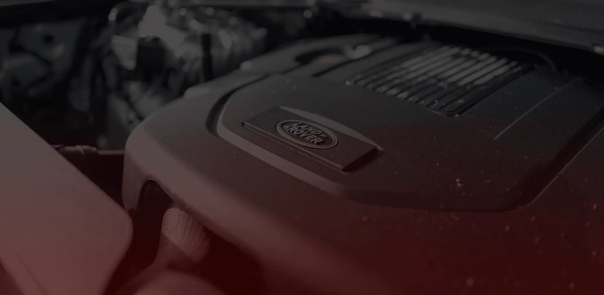 Close-up of a car engine, featuring the Land Rover logo on a sleek black cover. The image, reminiscent of what youd find in a Guelph mechanics garage, is enhanced by a dark, moody filter with a subtle red tint. Euro Mechanic | Brock Road Garage Guelph | Top Reviewed Auto Repair Shop in Guelph | Visit brockroadgarage.ca