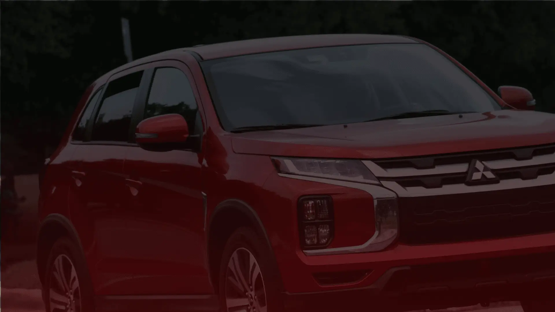 A red Mitsubishi SUV, expertly maintained by a skilled Mitsubishi mechanic in Guelph, is parked outdoors with trees in the background. The cars front and side are visible, featuring modern headlights and a sleek design. EuroMechanic | Brock Road Garage Guelph | Top Reviewed Auto Repair Shop in Guelph | Visit brockroadgarage.ca
