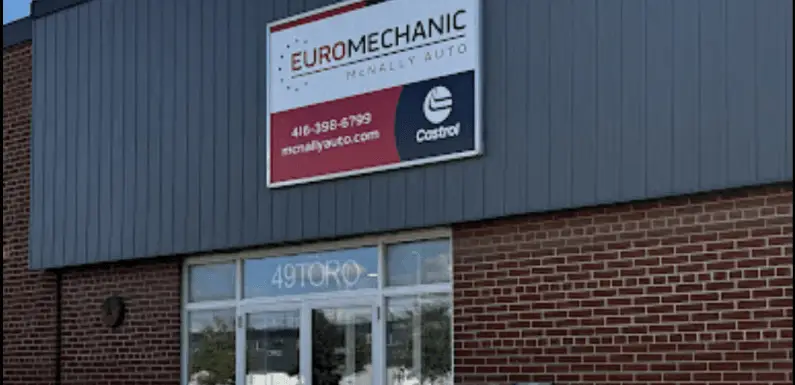 A brick building with a gray panel on top features a sign reading Euromechanic McNally Auto at the Brock Road Garage, complete with a phone number and website. Below the sign is a large windowed entrance with the partially visible number 4910RO. Euro Mechanic | Brock Road Garage Guelph | Top Reviewed Auto Repair Shop in Guelph | Visit brockroadgarage.ca