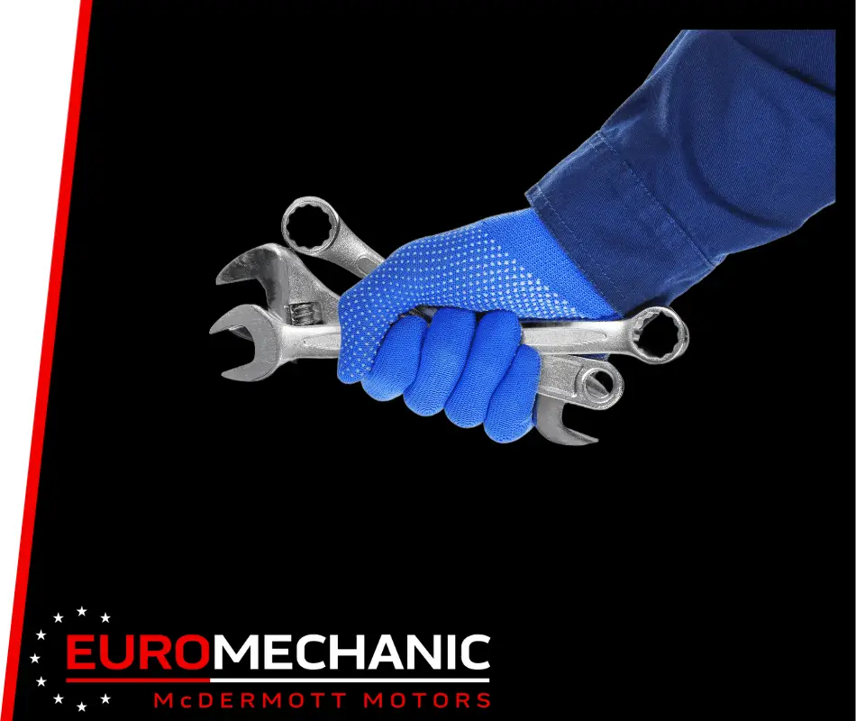 A gloved hand in a blue mechanics uniform holds several wrenches, ready for preventative maintenance. The black background highlights the logo at the bottom: EURO MECHANIC - MCDERMOTT MOTORS, known for expert car repair in Guelph, with a stylized star design. Euro Mechanic | Brock Road Garage Guelph | Top Reviewed Auto Repair Shop in Guelph | Visit brockroadgarage.ca