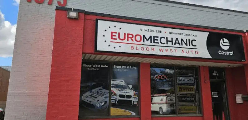 The image depicts the exterior of Euro Mechanic Bloor West Auto, reminiscent of a Brock Road Garage. The red and white building boasts a sign with contact details and a Castrol logo. A large display window showcases a car image alongside various auto service advertisements. Euro Mechanic | Brock Road Garage Guelph | Top Reviewed Auto Repair Shop in Guelph | Visit brockroadgarage.ca